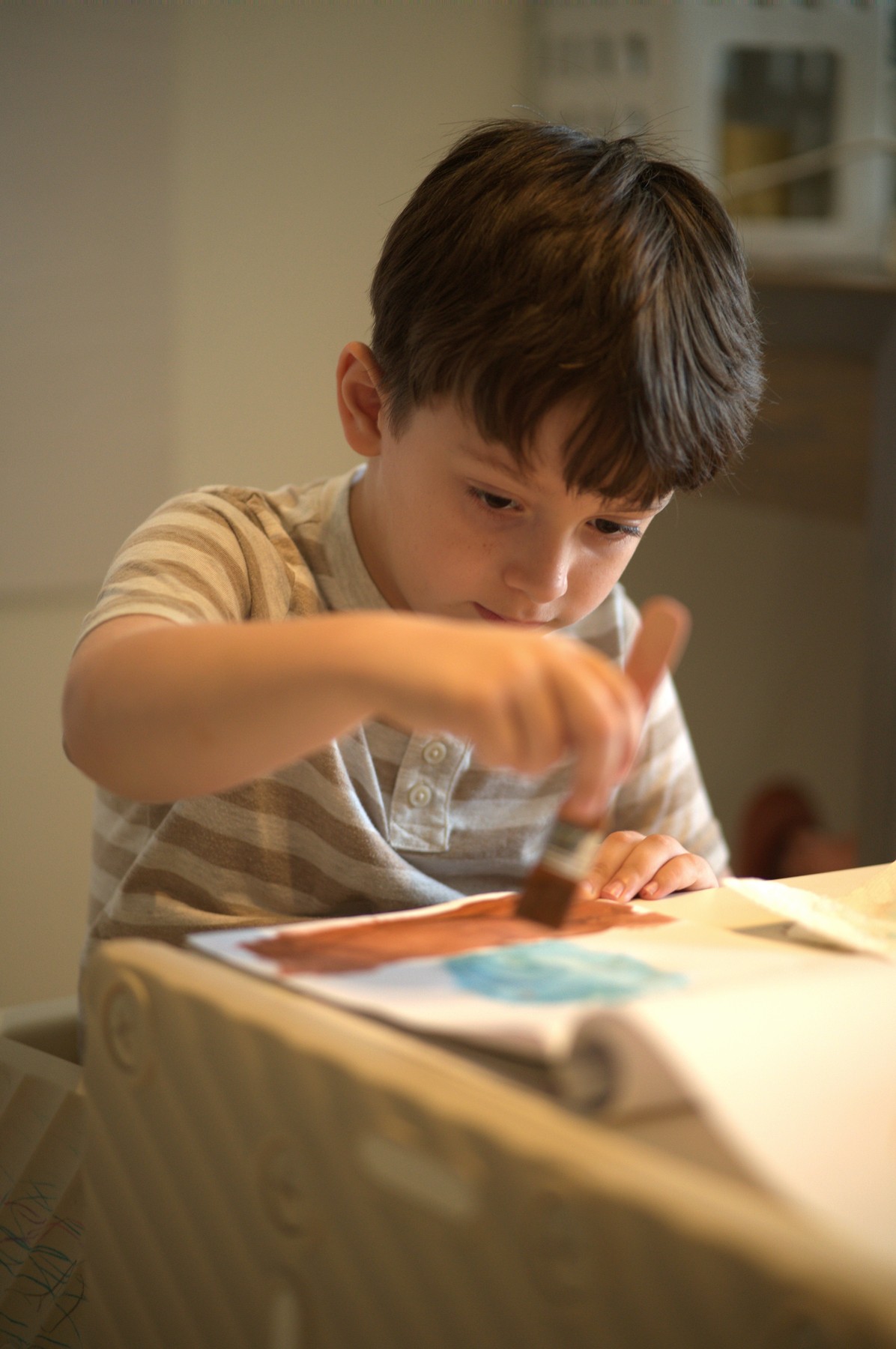 Lucas leaning right over the same sheet, the wide brush mid-stroke in the rust-red shape, his free hand flat on the paper to hold it steady