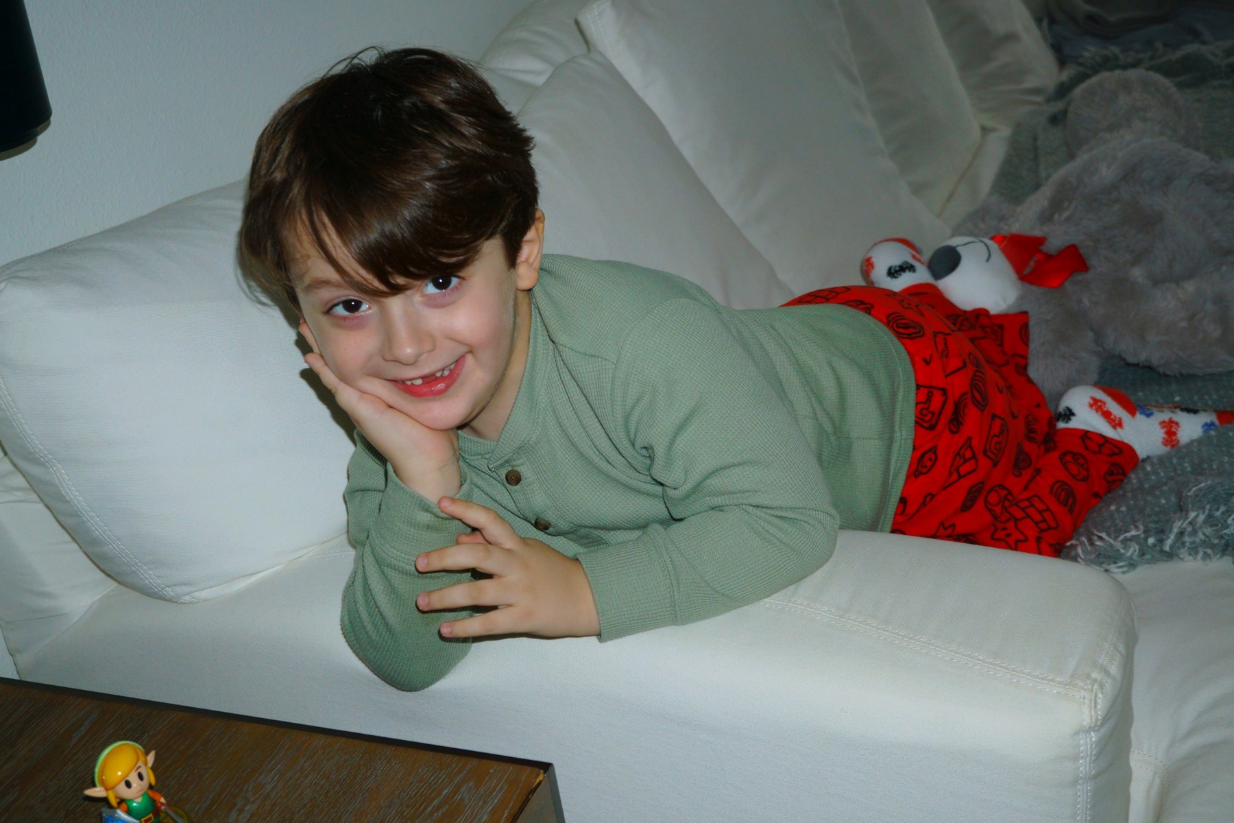 Lucas stretched on his stomach along the white couch, chin propped on one hand, grinning slyly at the camera