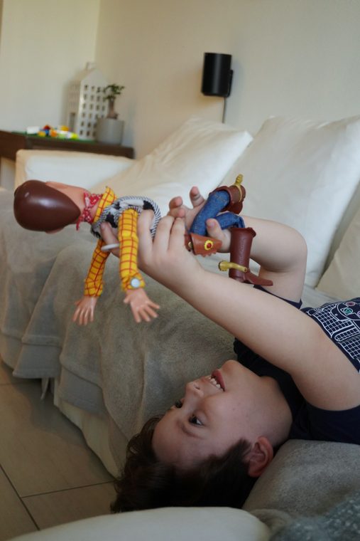 Lucas acostado al revés en el sofá, riéndose, sosteniendo a Woody también al revés sobre su cara